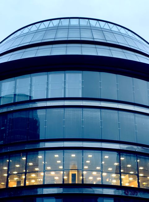 Two professional window cleaners wearing safety helmets and harnesses are performing surface cleaning on the exterior glass windows of a high-rise office building. The workers are suspended by ropes a